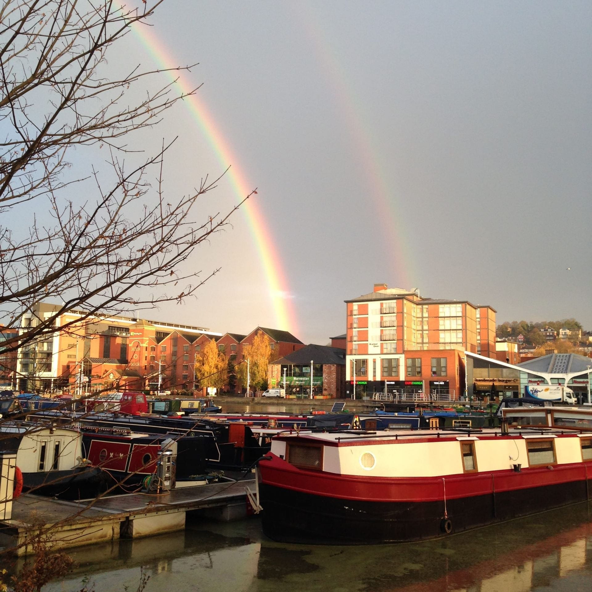 Two rainbows, above buildings and boats across the Brayford Pool.
