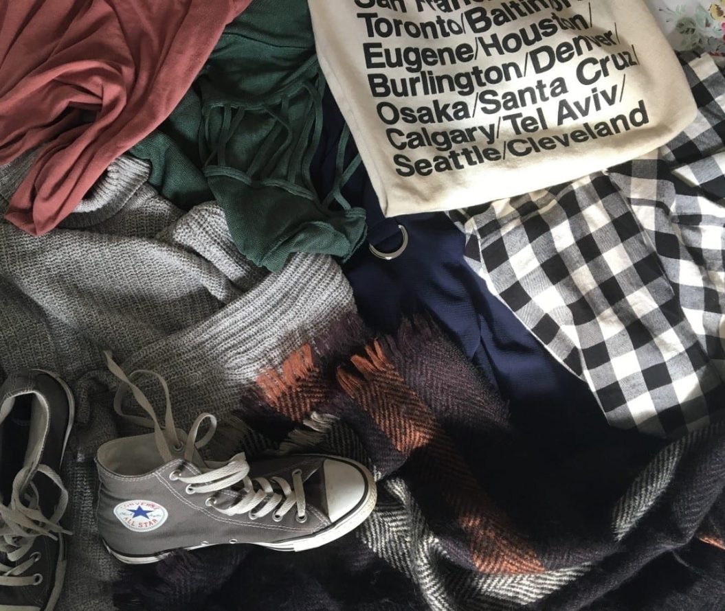 Pile of clothes, tote-bag and converse shoes.
