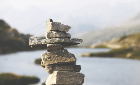 A stack of rocks balancing on top of each other, in front of a blurred river background.