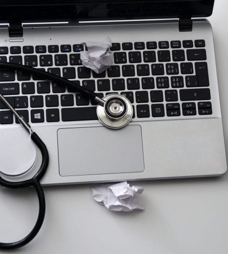 Open laptop, with a stethoscope, balled up pieces of paper, and a mouse.