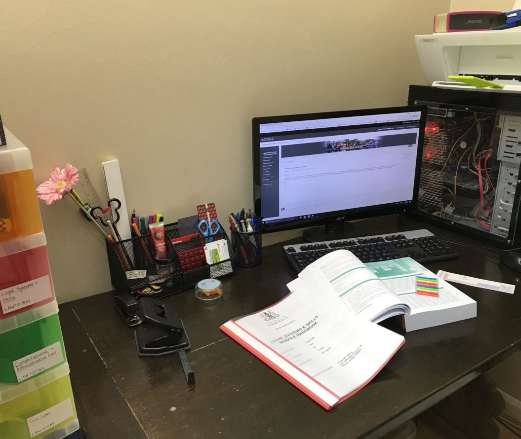 Desk with a computer, stationary and open text books.