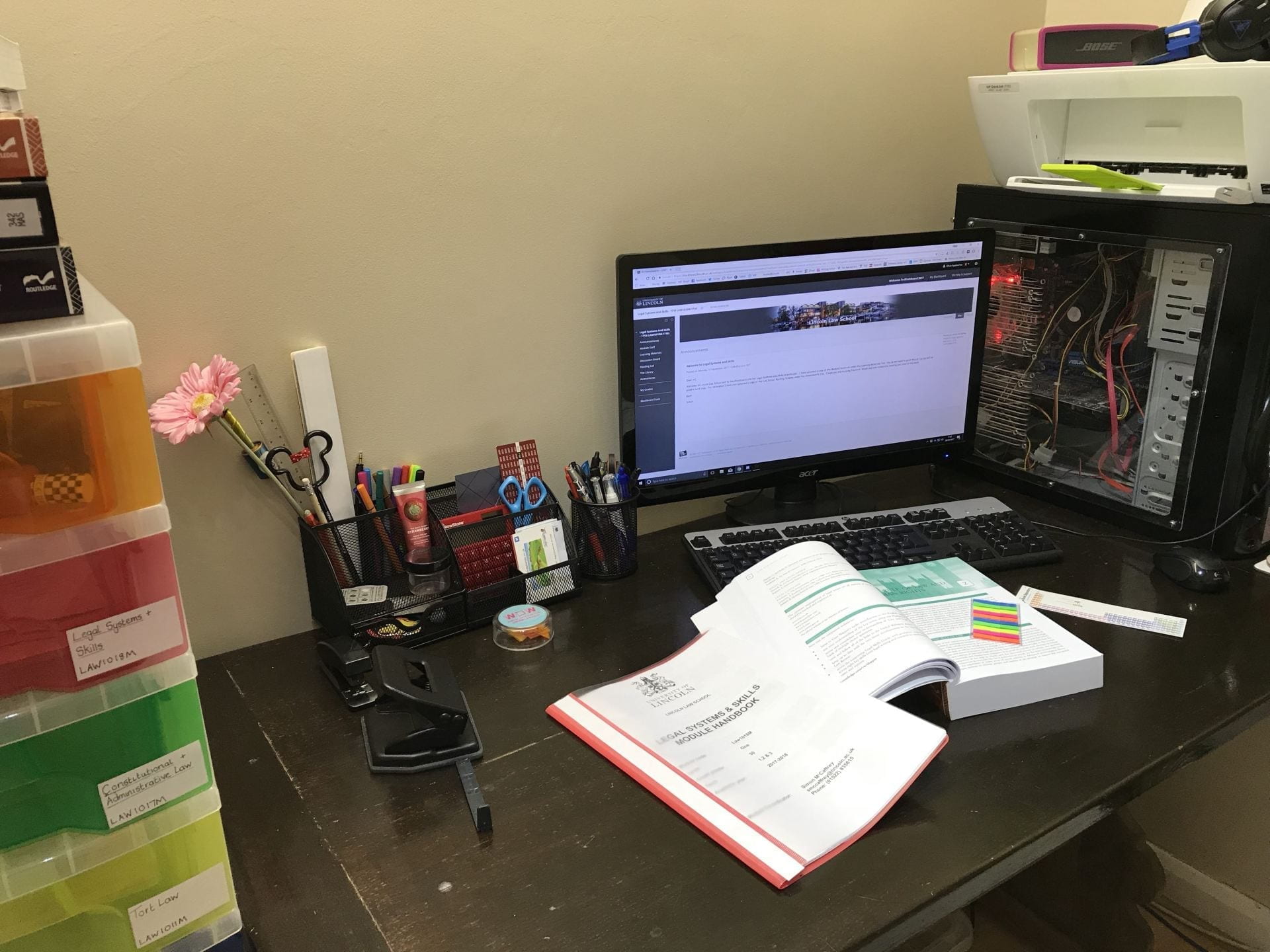 Desk with a computer, stationary and open text books.