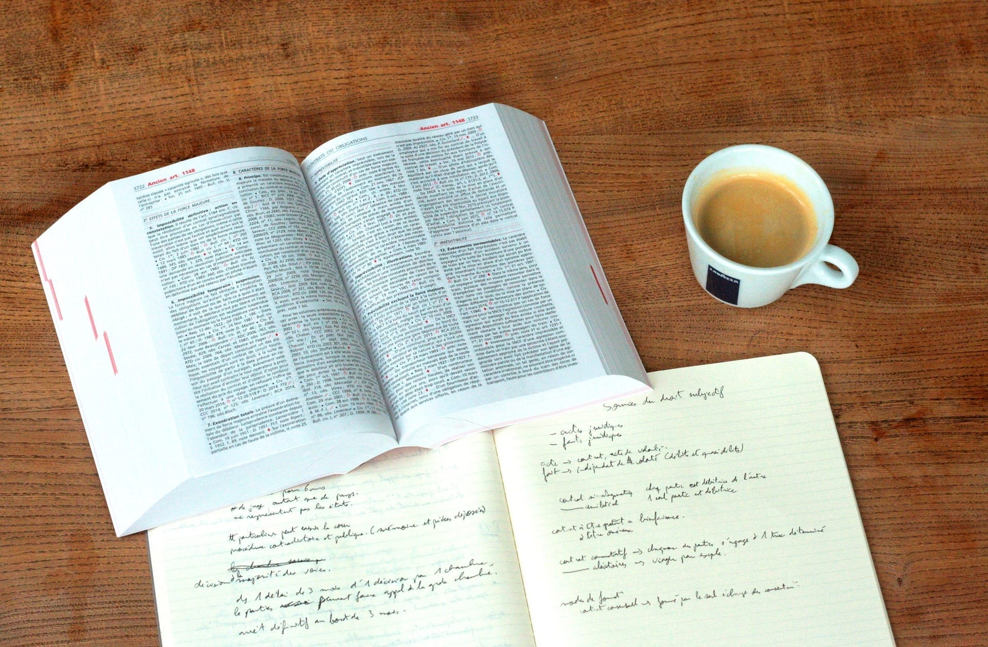 Open text book, notebook and a cup of coffee.