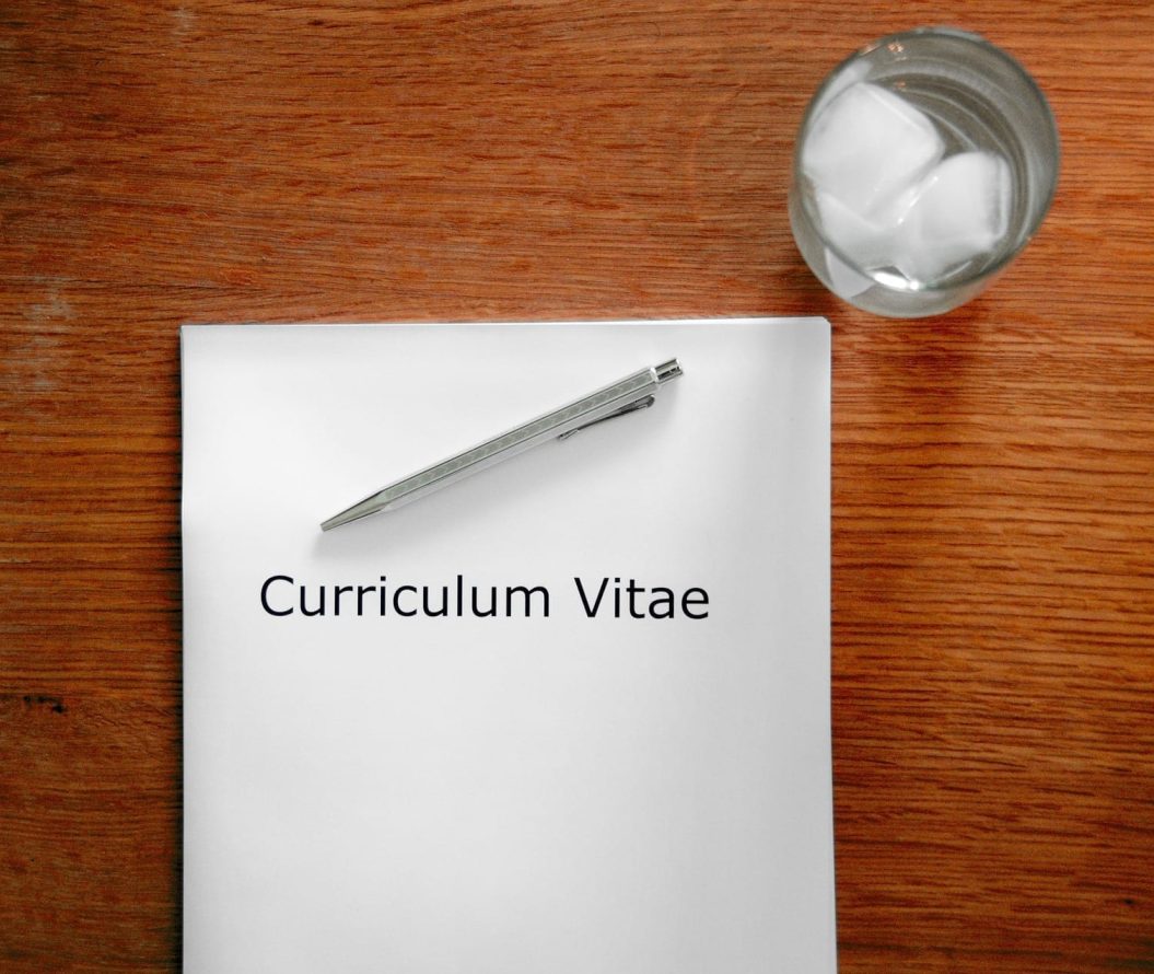 A white piece of paper, with Curriculum Vitae written on it, a pen and a glass of water.