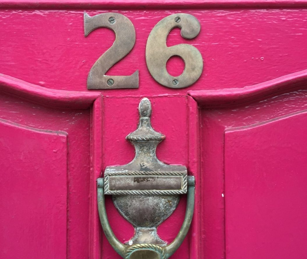 Pink door, with the number twenty six, over a door knocker.
