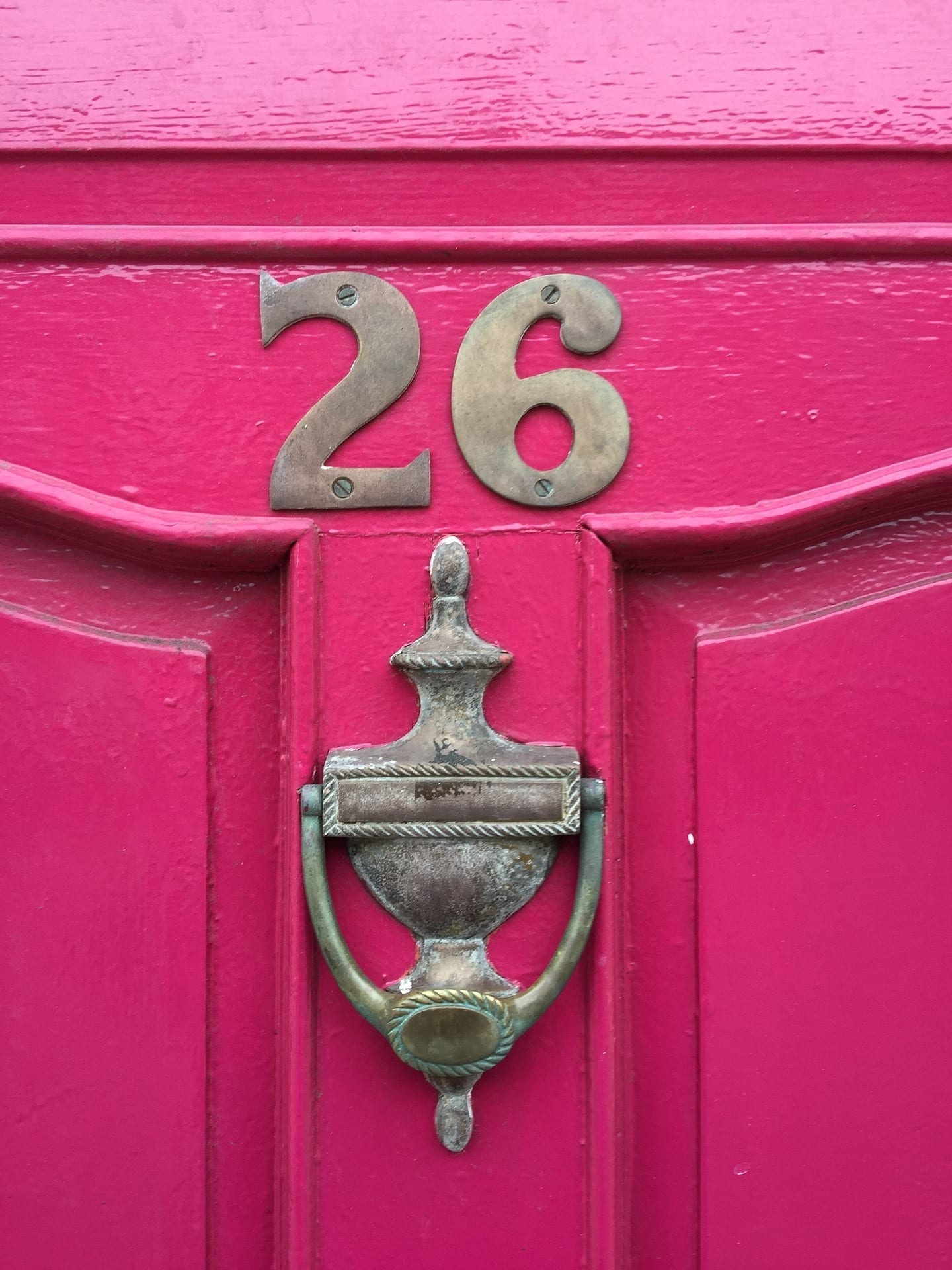 Pink door, with the number twenty six, over a door knocker.