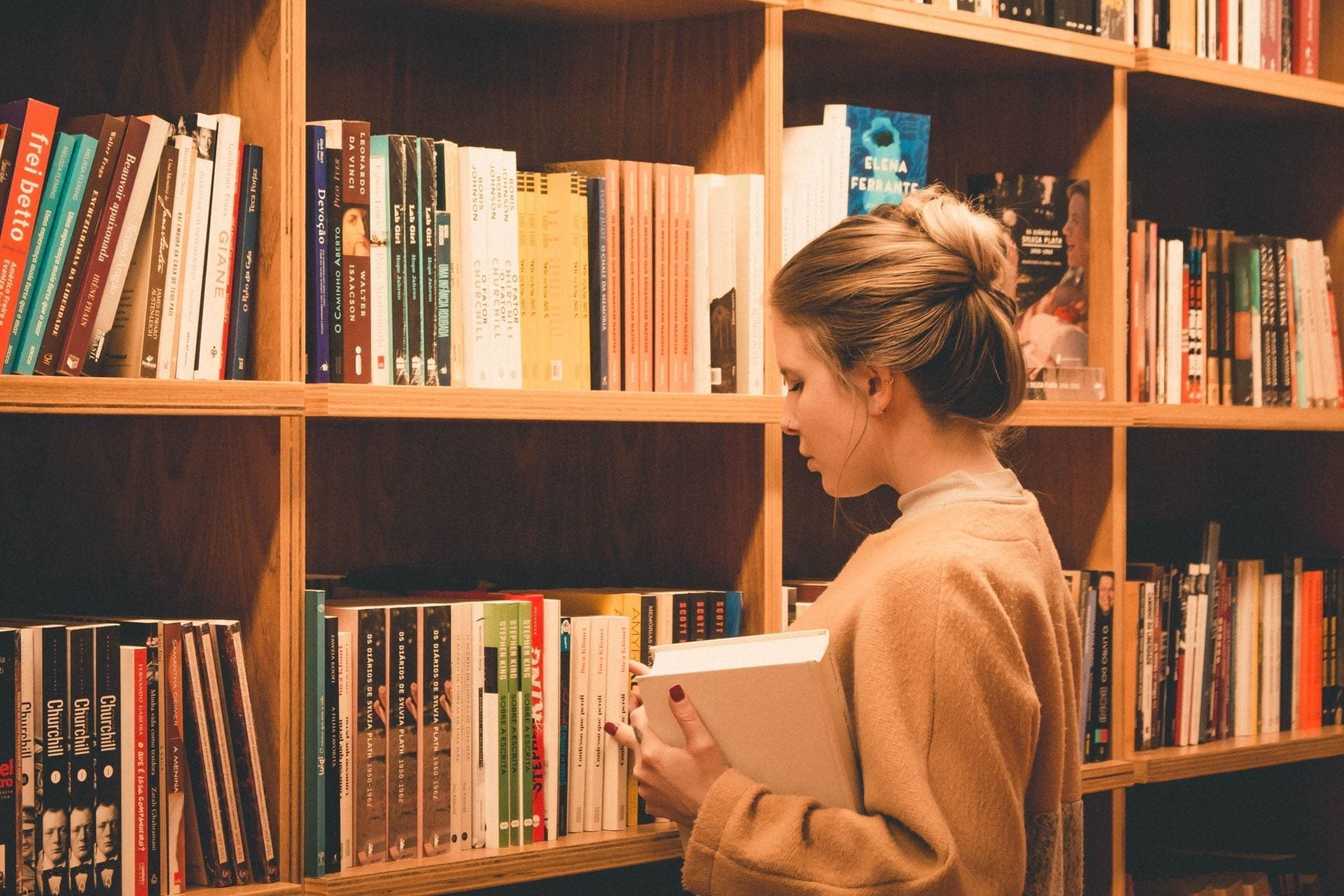 A girl stood in front of a bookshelf full of books, holding a book