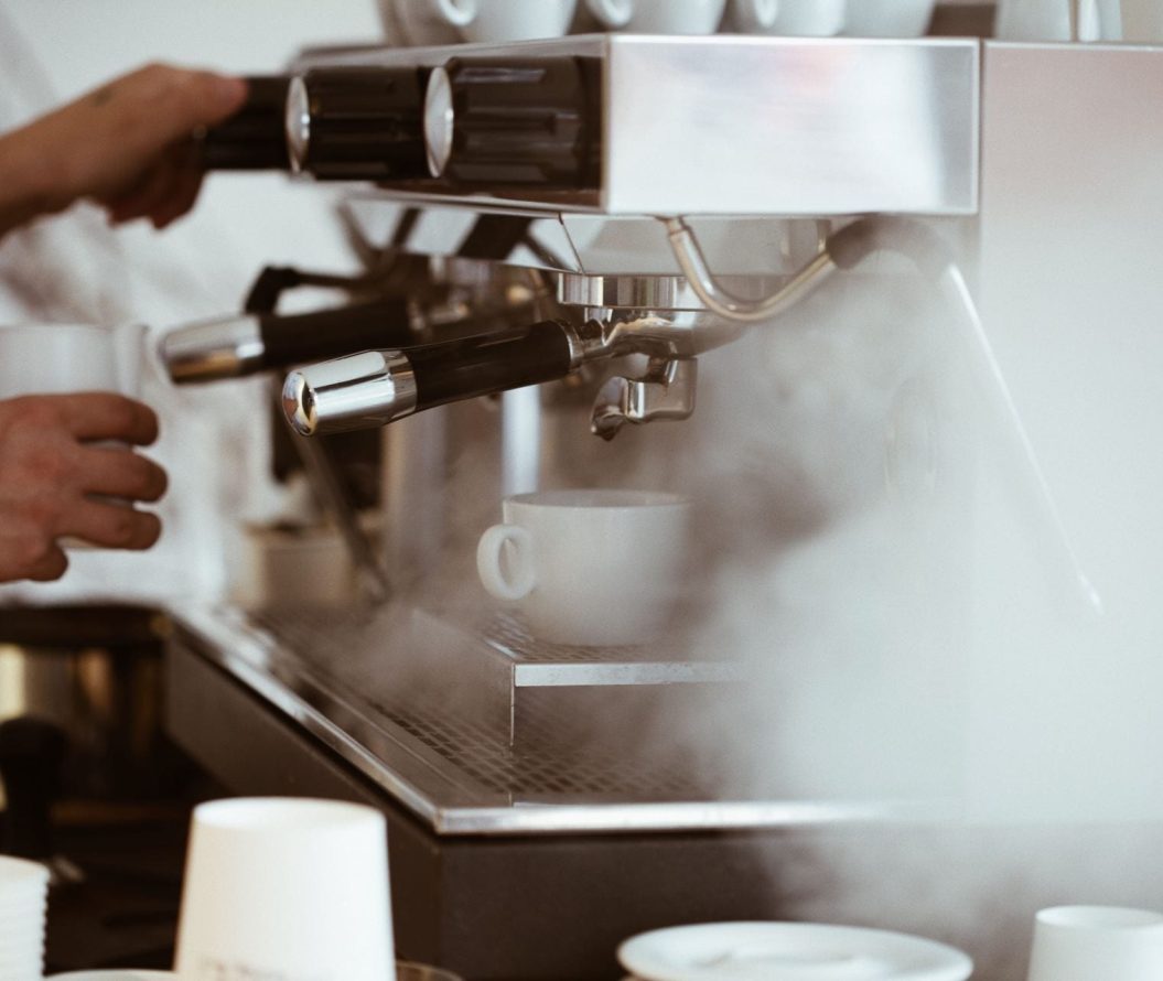 Close up of coffee machine steaming with a man frothing milk