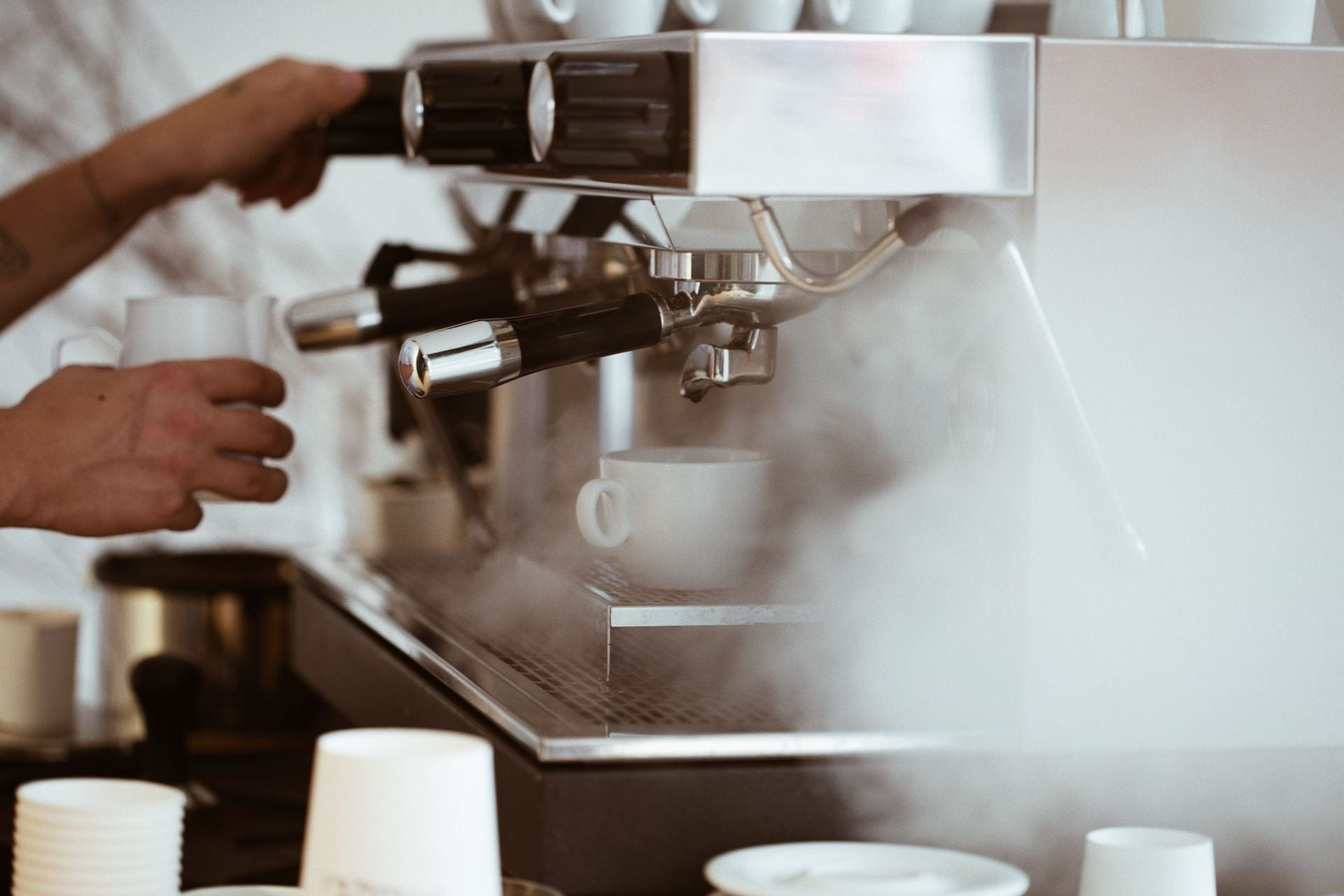 Close up of coffee machine steaming with a man frothing milk