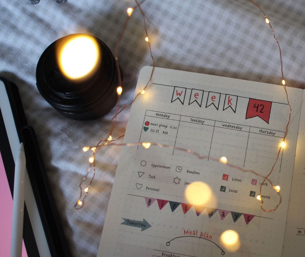 Week planner notebook open on a bed with and iPad and fairy lights