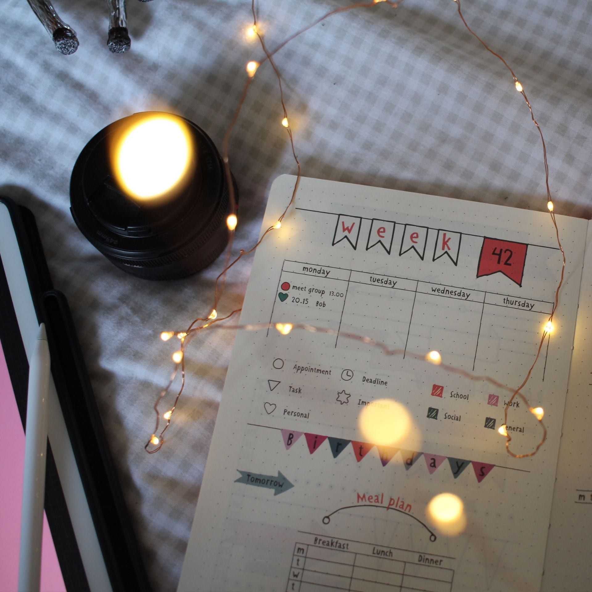 Week planner notebook open on a bed with and iPad and fairy lights