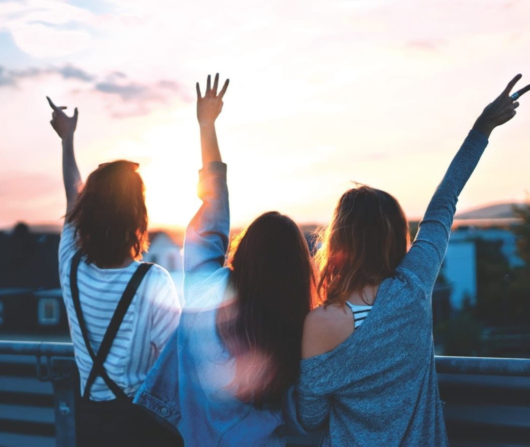 Three girls looking out over a skyline with their arms in the air