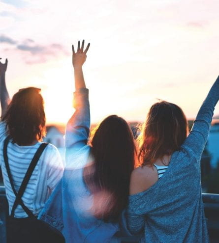 Three girls looking out over a skyline with their arms in the air