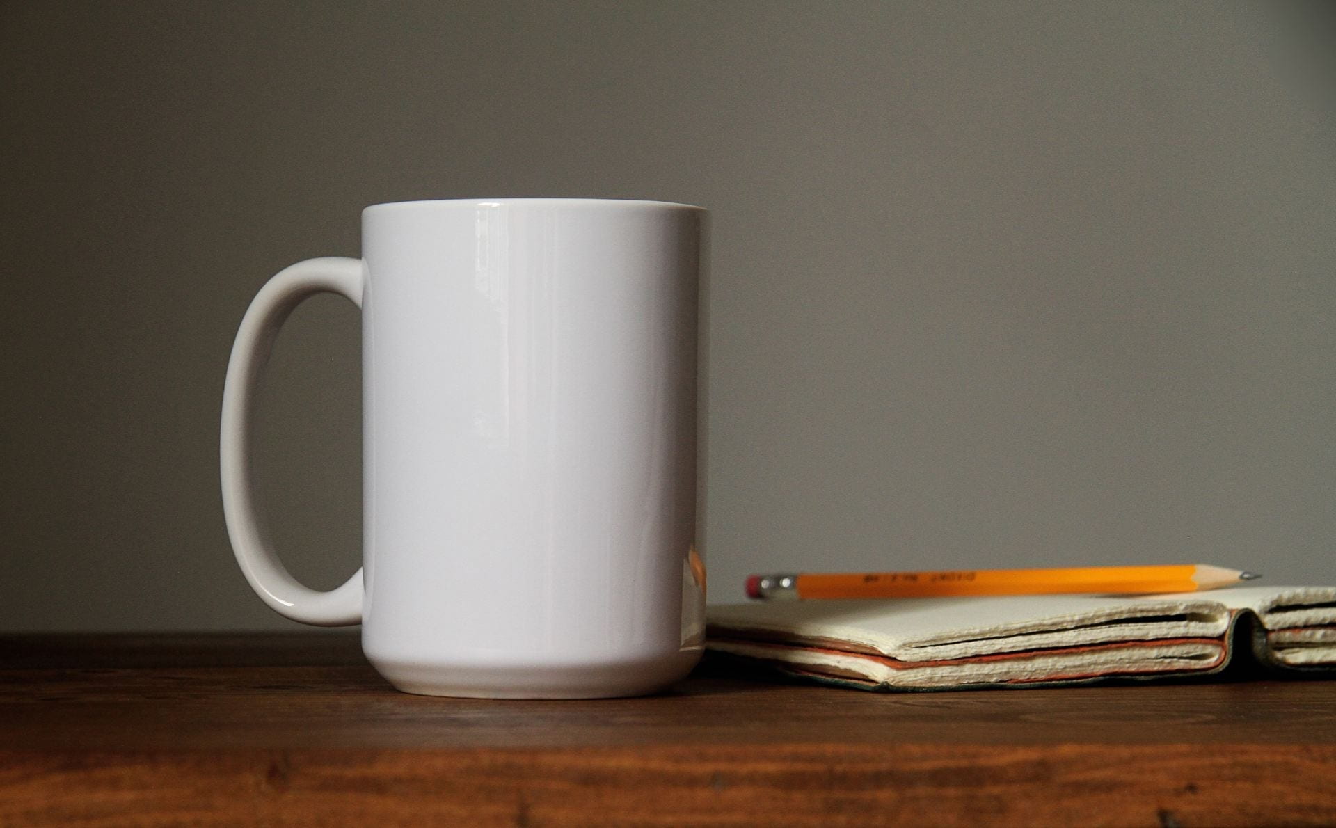 A mug on a table next to a notebook and pencil