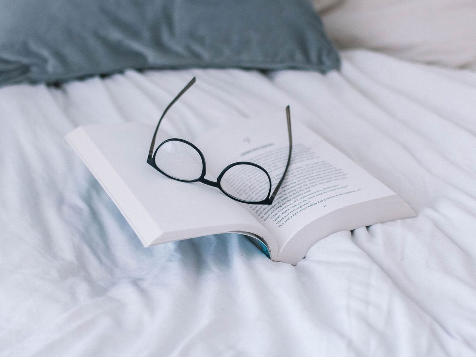 A pair of glasses lying on a book on top of a bed
