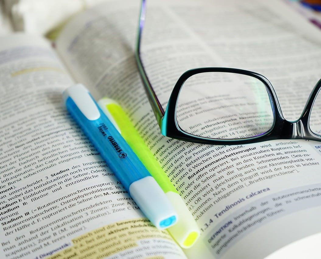 A pair of glasses and two highlighters rest on an open book