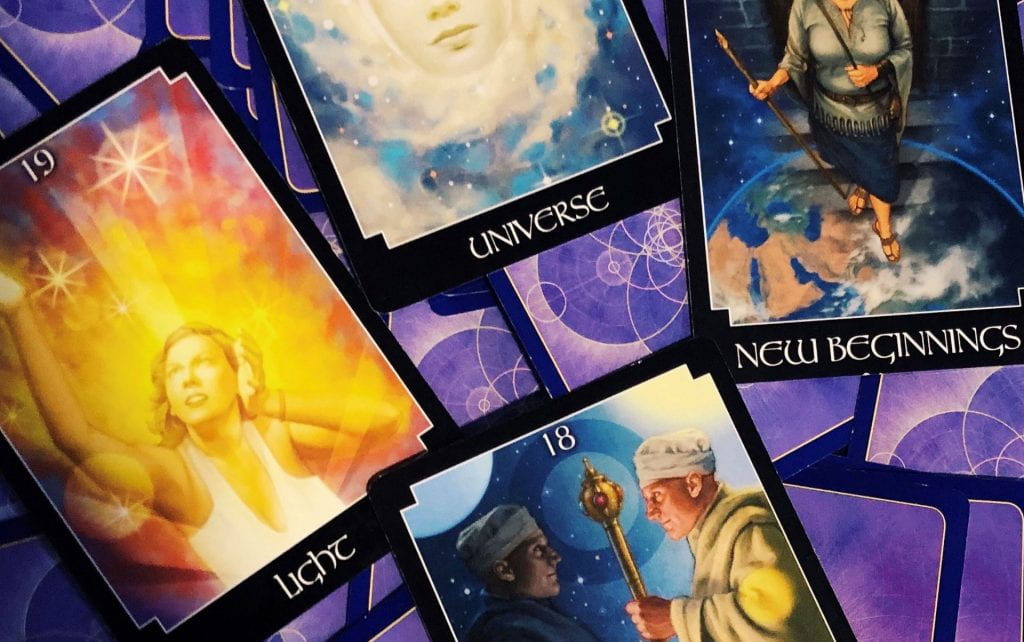 Selection of tarot cards on a purple backdrop saying "light", "universe" and "new beginnings".