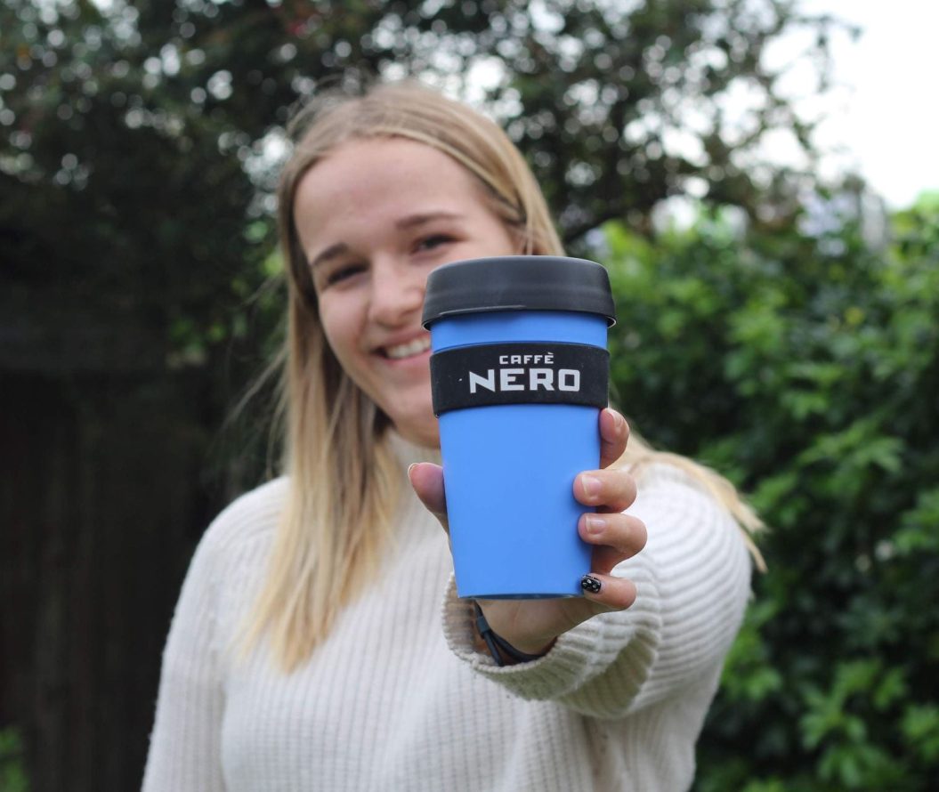 woman smiling and holding caffe nero cup in a park