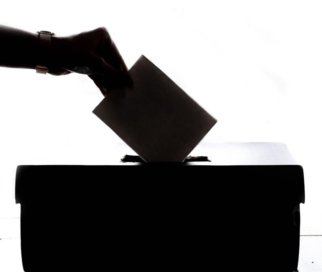 Close-up of a hand putting a poll slip into a hole in a box.
