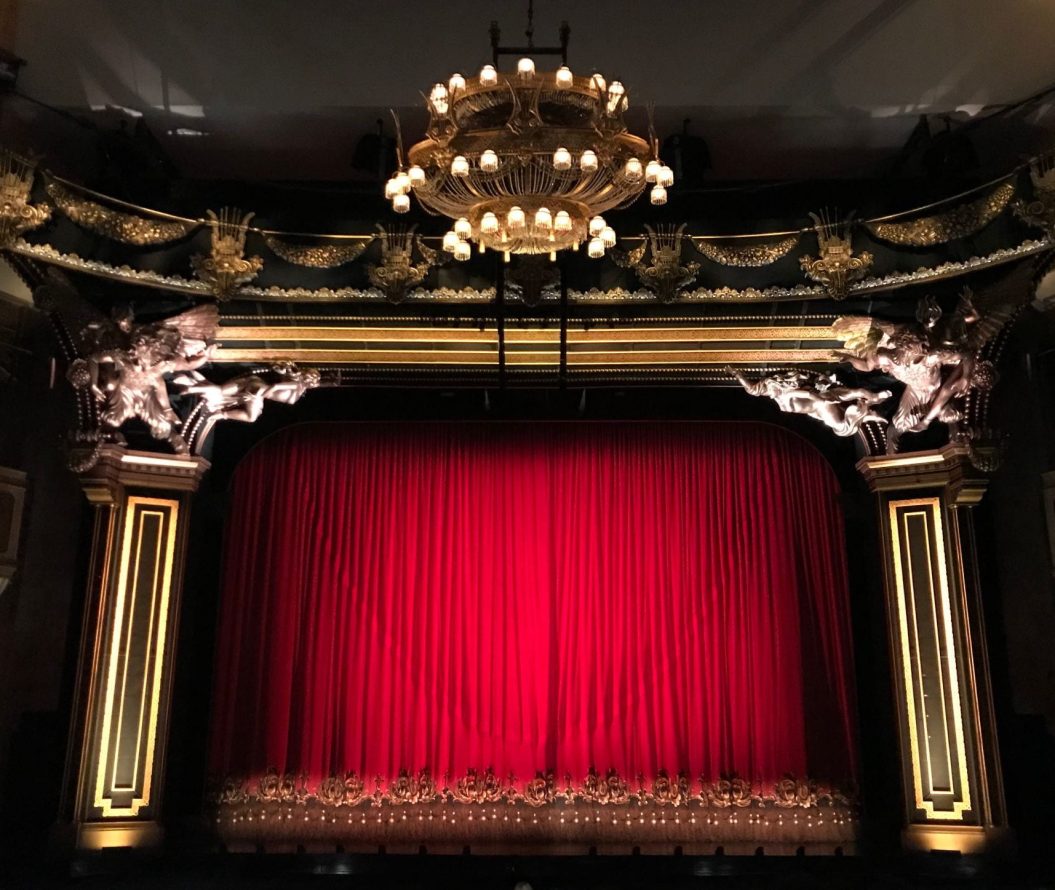 A photo depicting a theatre, with a red curtain closed across the stage.
