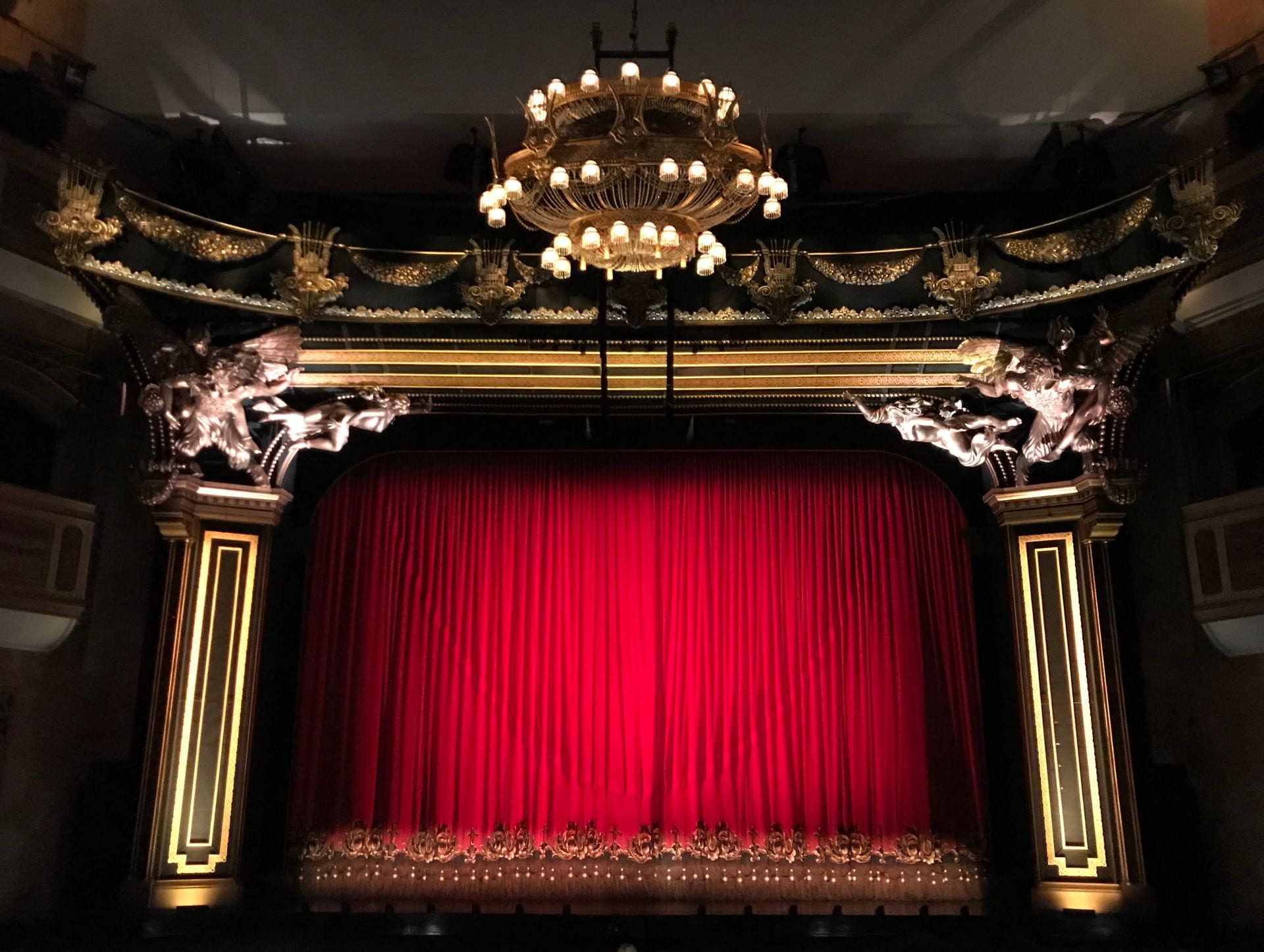 A photo depicting a theatre, with a red curtain closed across the stage.