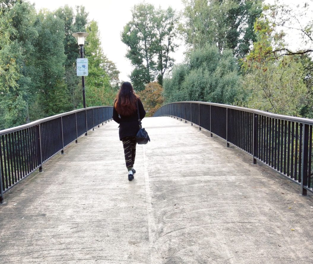 woman walking over bridge surrounded by a lamp post and trees