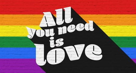 a sign saying 'all you need is love' with pride colours in background