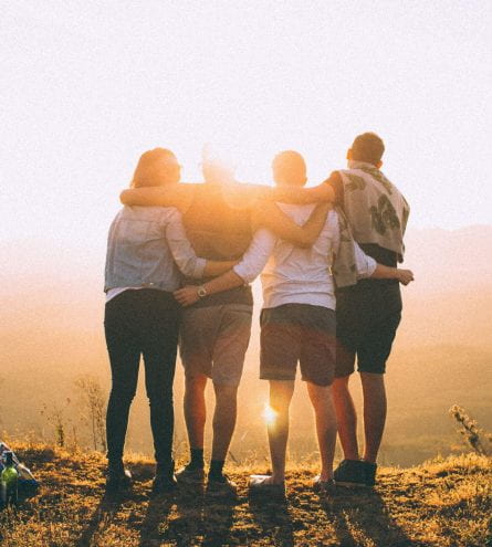 Four people linking arms looking at sunset.