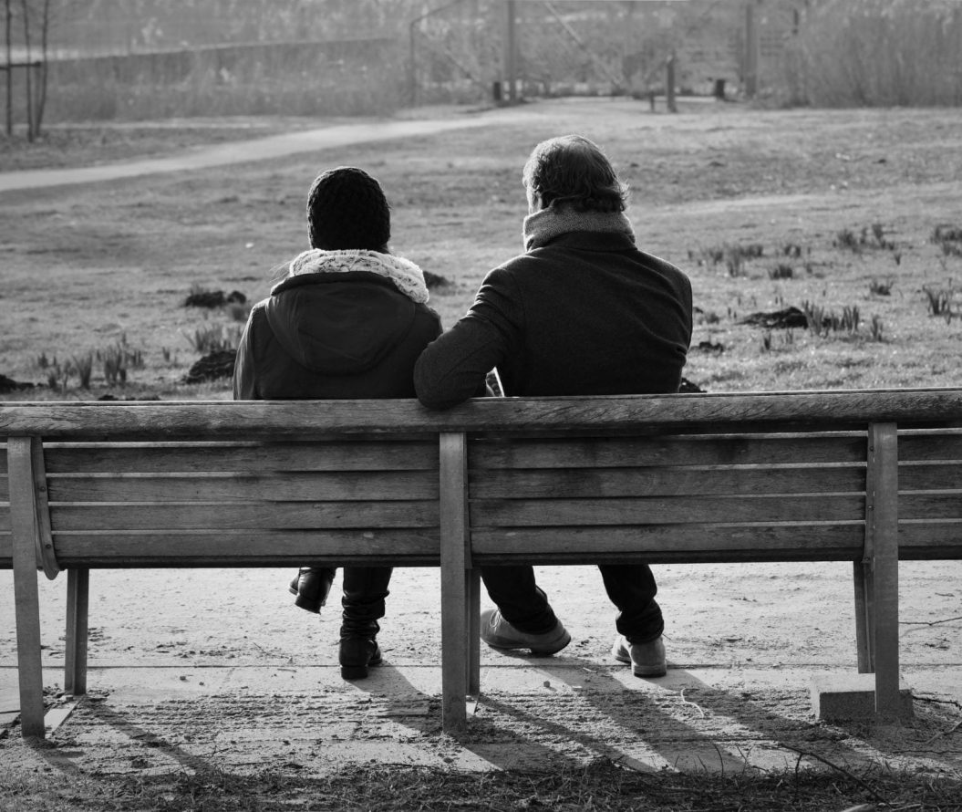 two people sat on a bench in a park, black and white