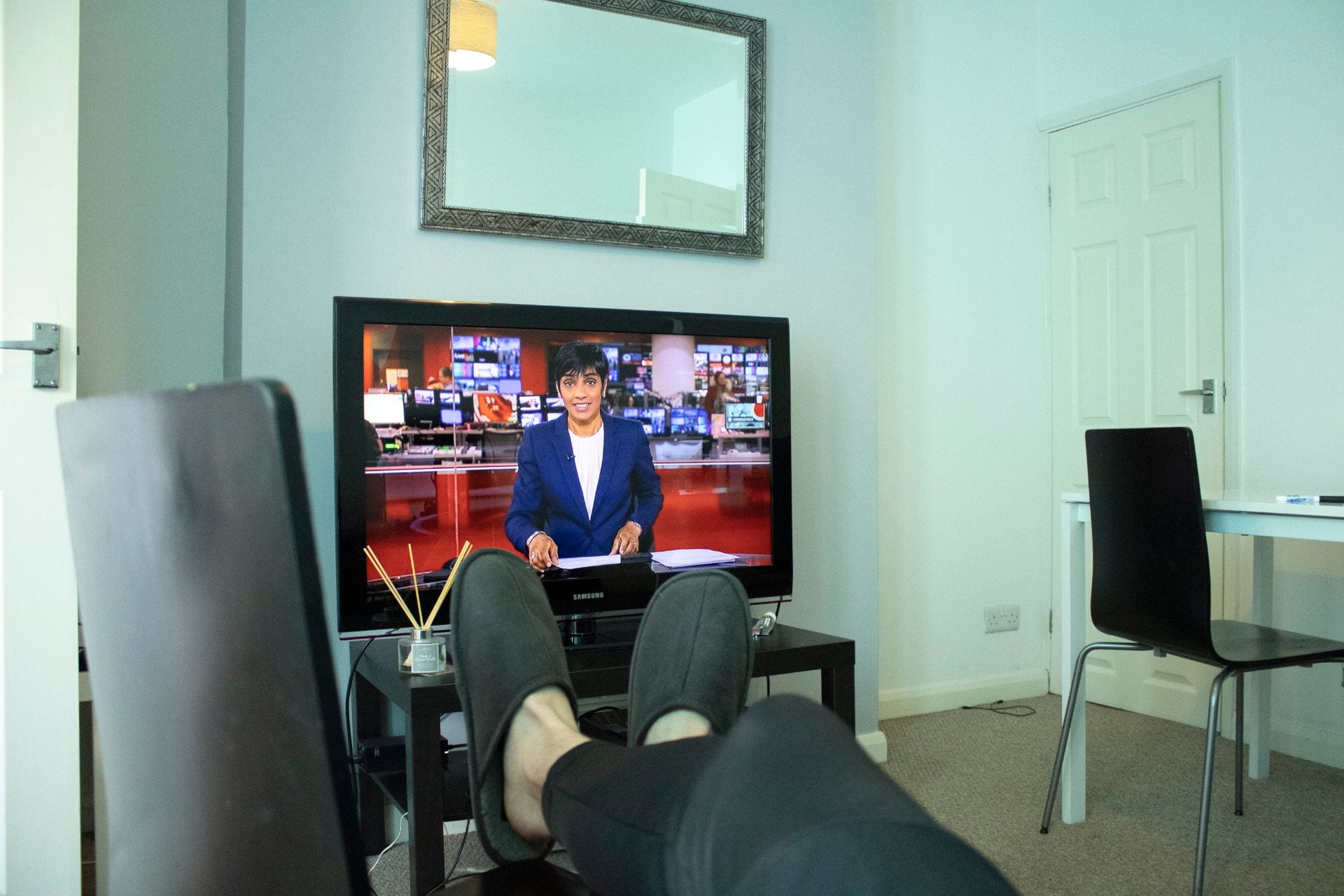 A man with his feet up whilst watching BBC news.
