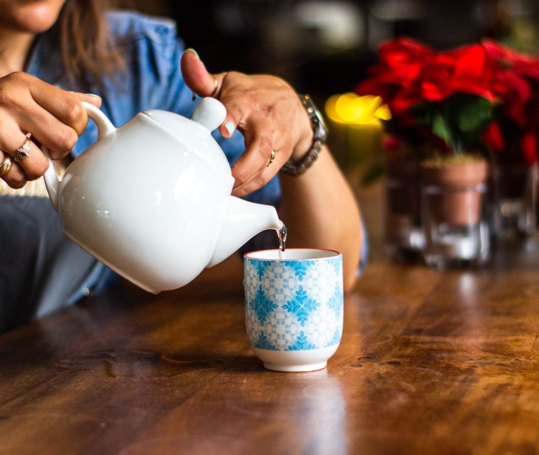 A lady pouring tea from a teapot into a mug