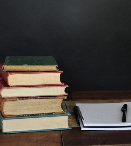 Stack of books on a desk next to an open notebook