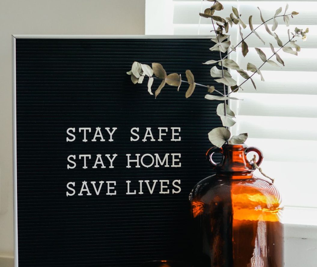 Framed photograph that reads: Stay Safe, Stay Home, Save Lives. Potted plant and a candle are in the foreground of the image.