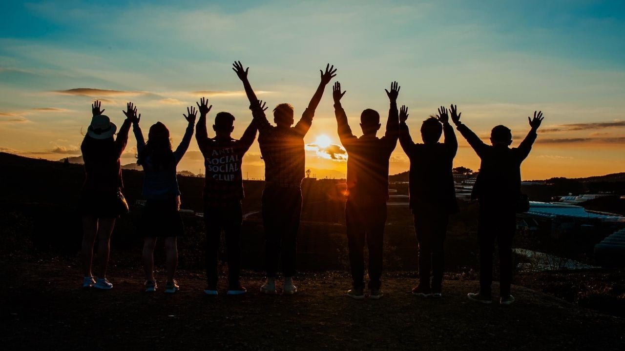 silhouettes of 7 people with their hands in the air watching the sunset