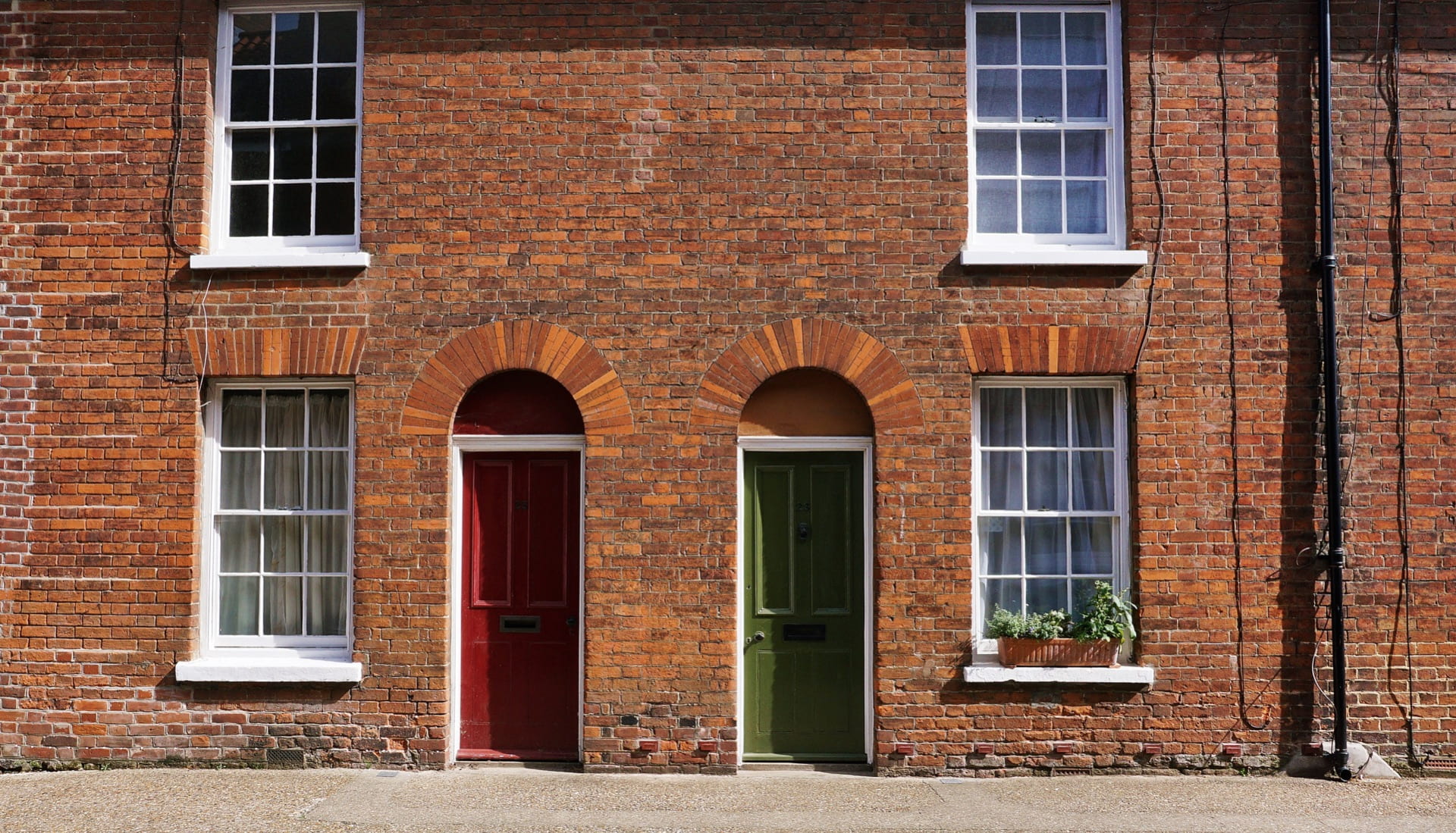 Front on photo of the exterior of a terraced house featuring a green and a red door