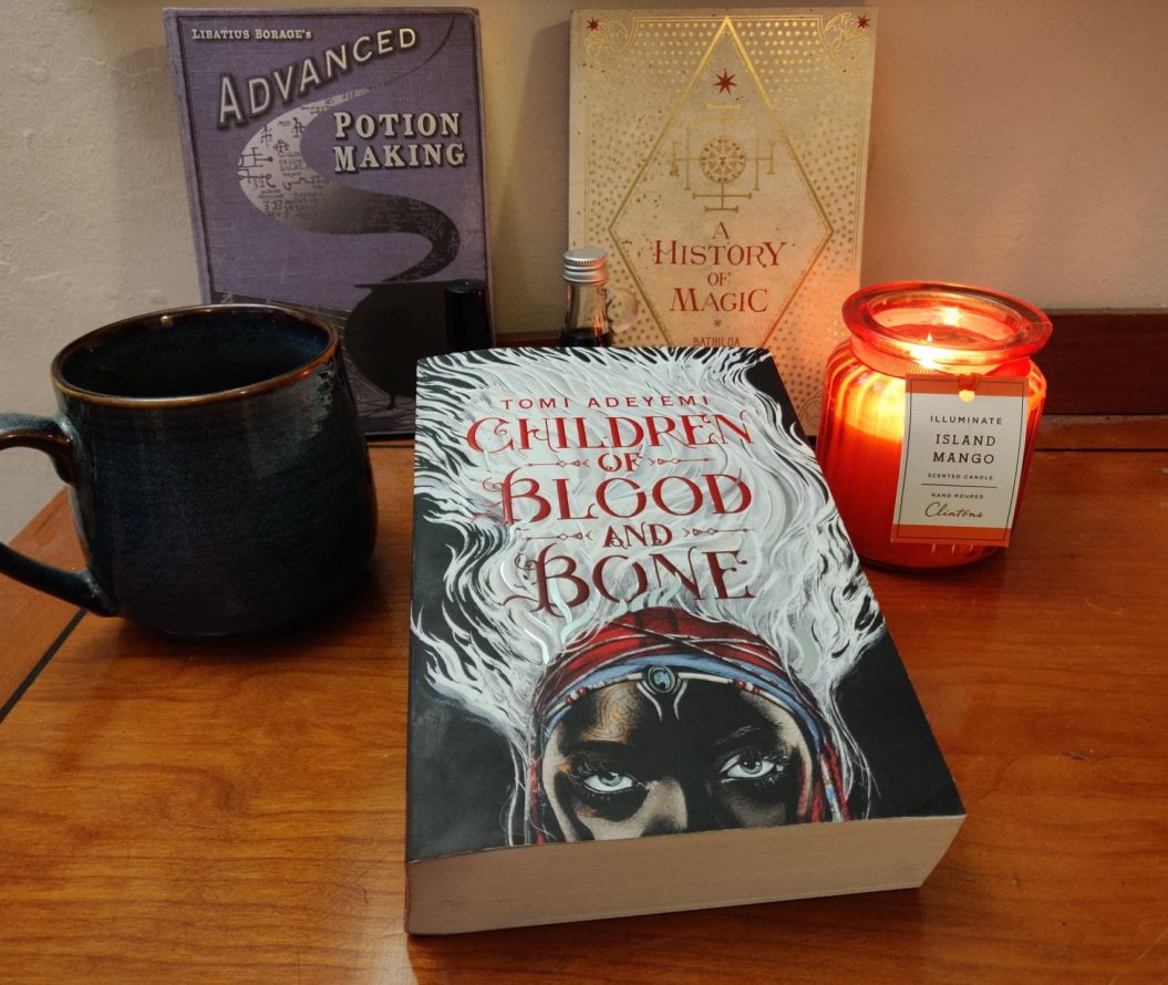 Focal book of 'Children of Blood and Bone' by Tomi Adeyemi next to a candle and a mug