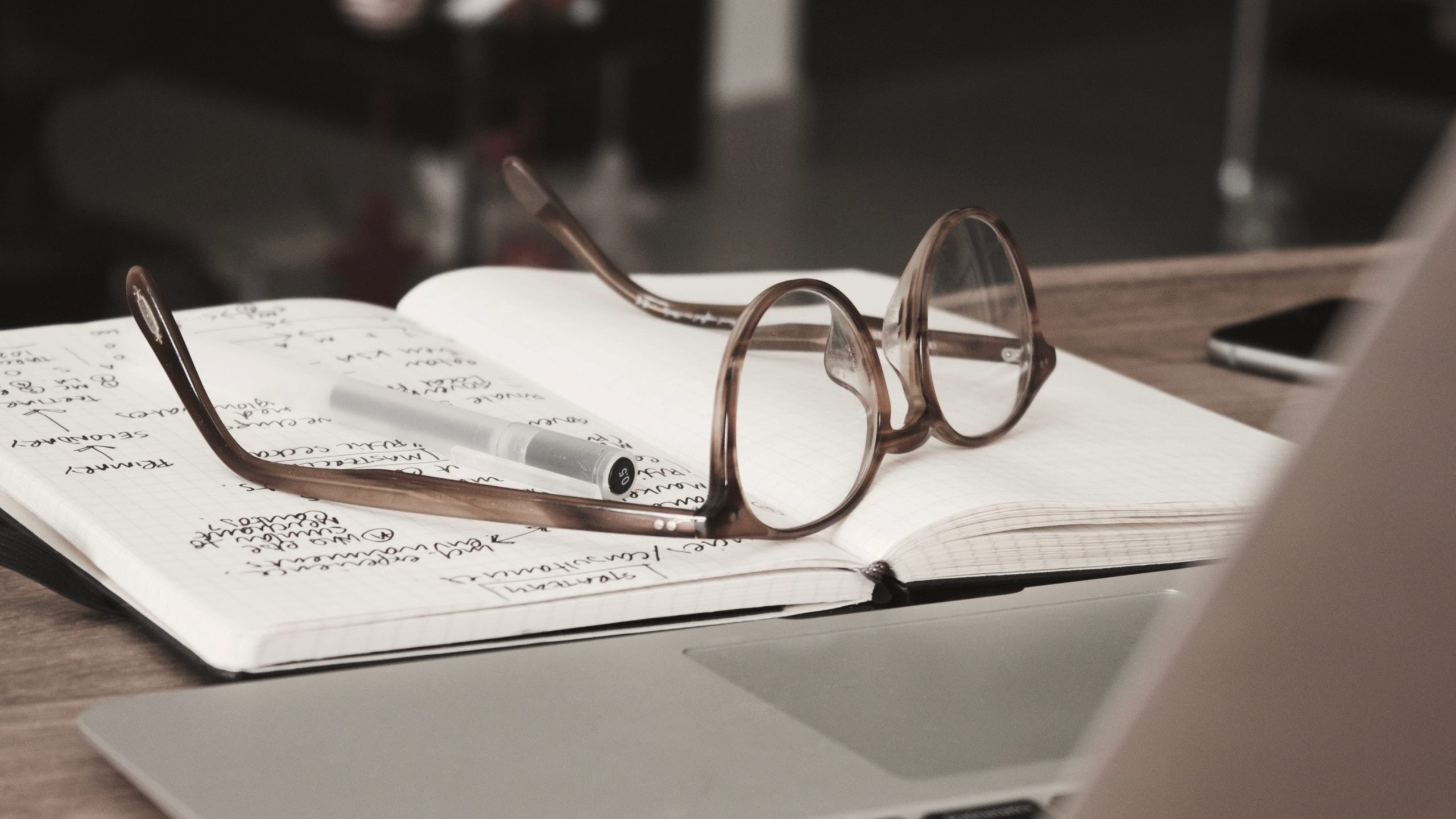 A pair of glasses on an notebook in front of a laptop