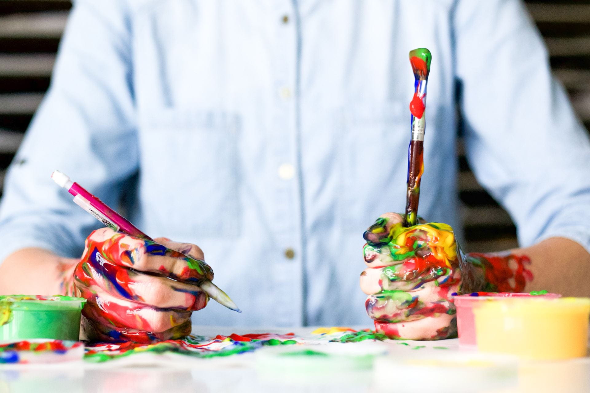Someone holding an upside down paintbrush and a ben, covered in colourful paint