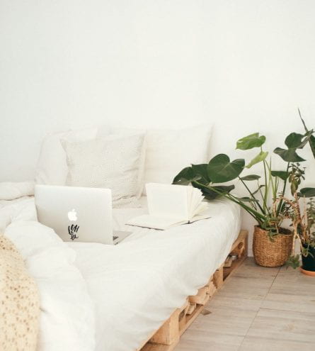 An organised white bed with a laptop and plants