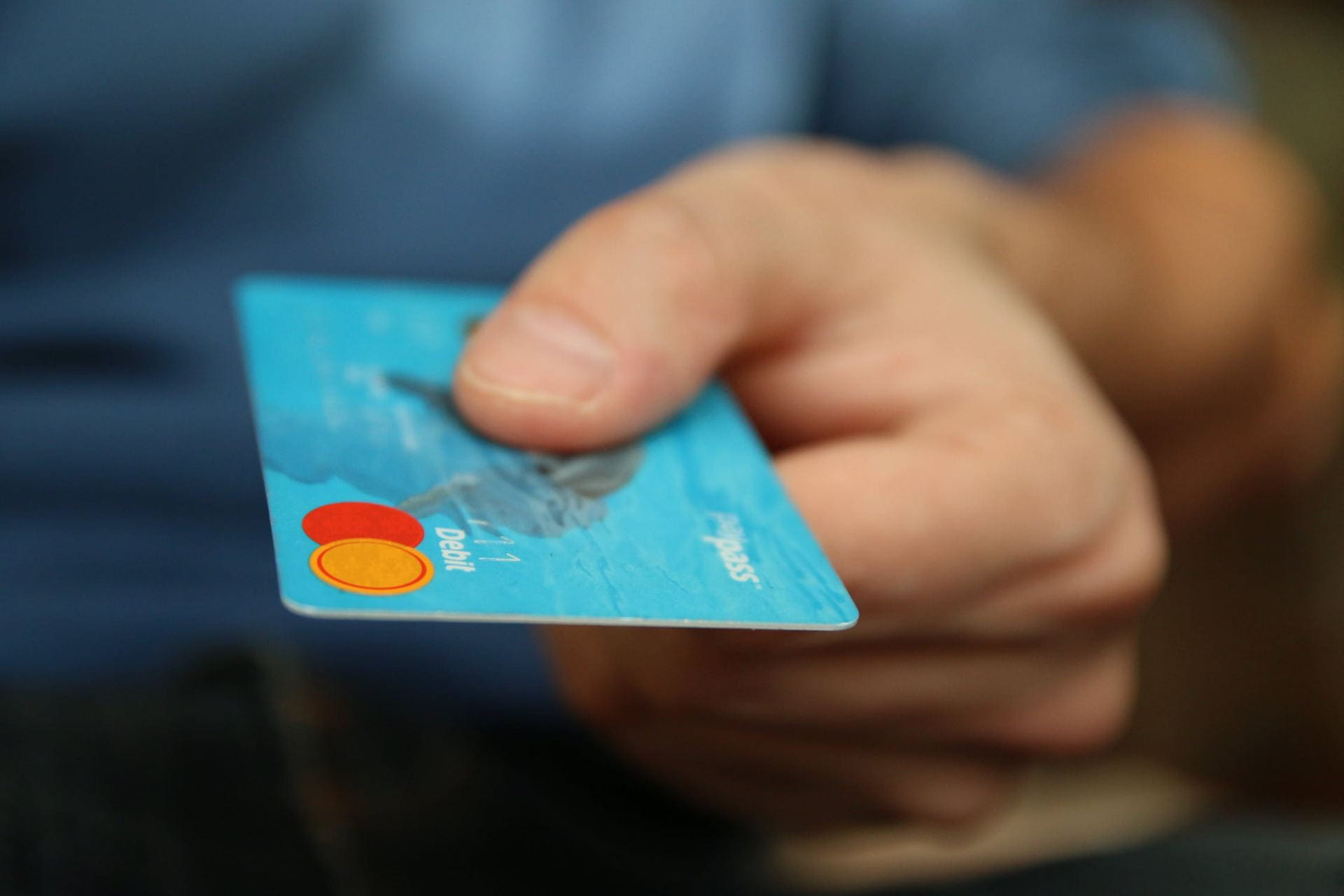 A hand holding a debit card forward.