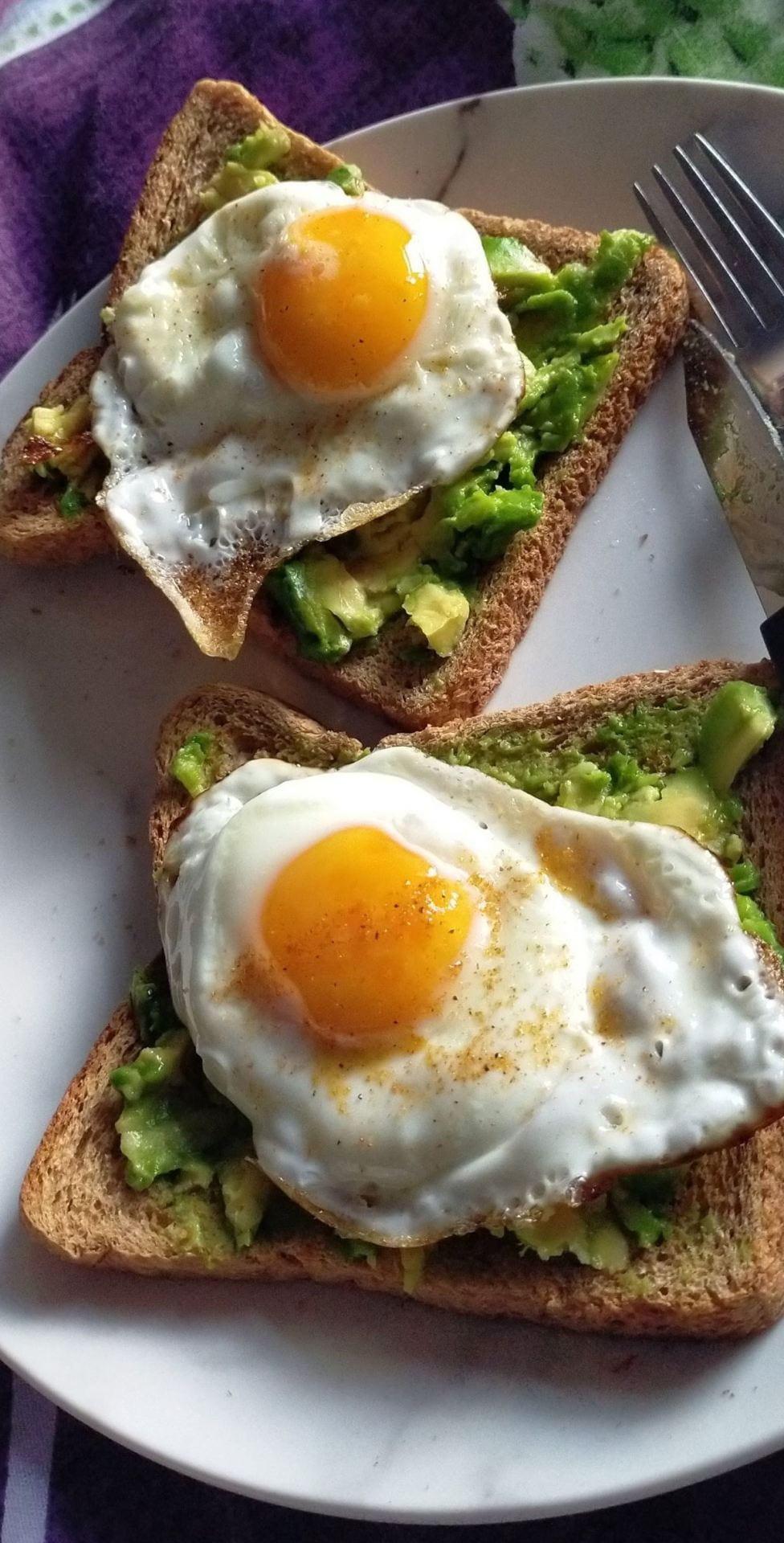 Two slices of toast with smashed avocado and a fried egg on top of them.