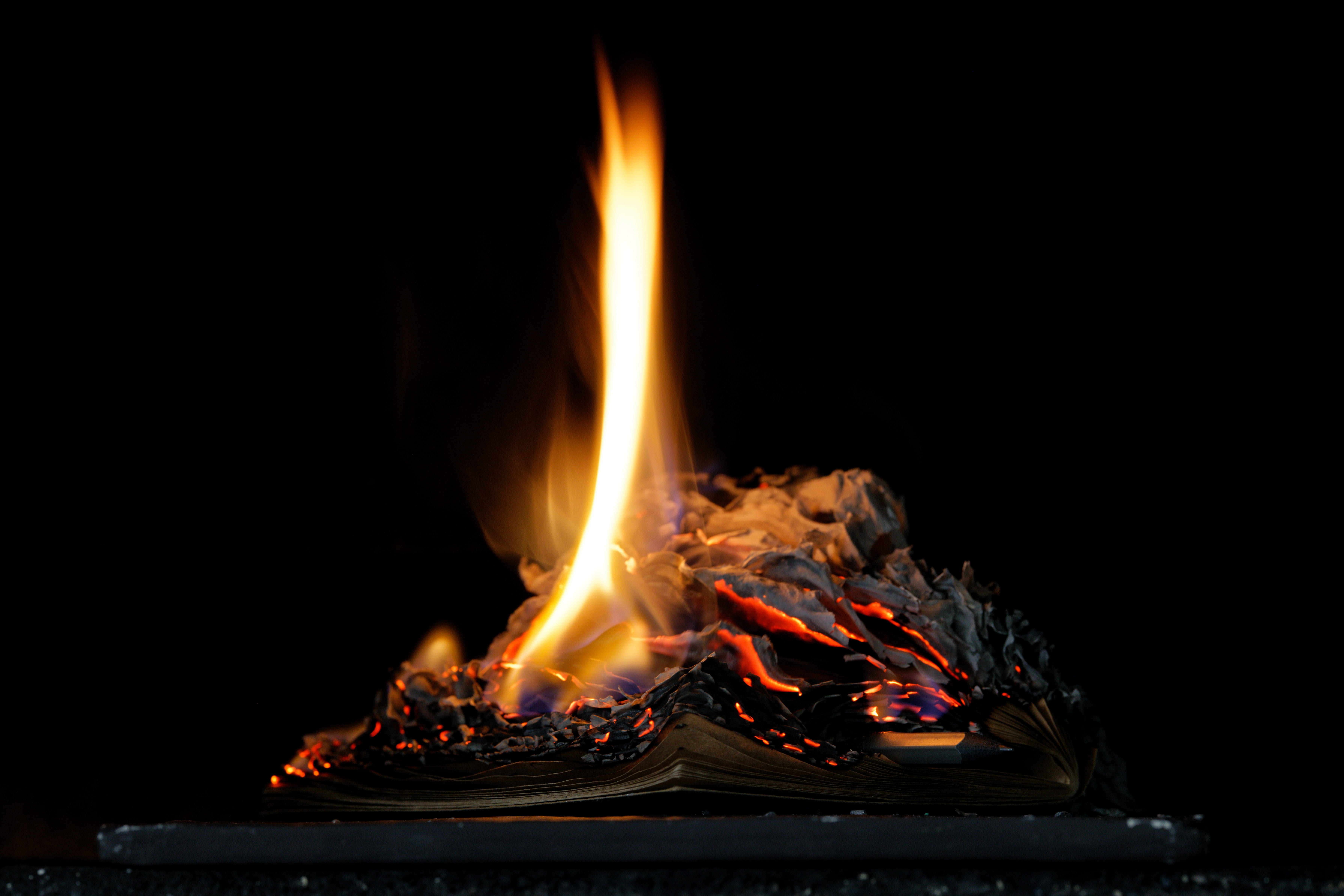A small stack of paper on fire against a black background.