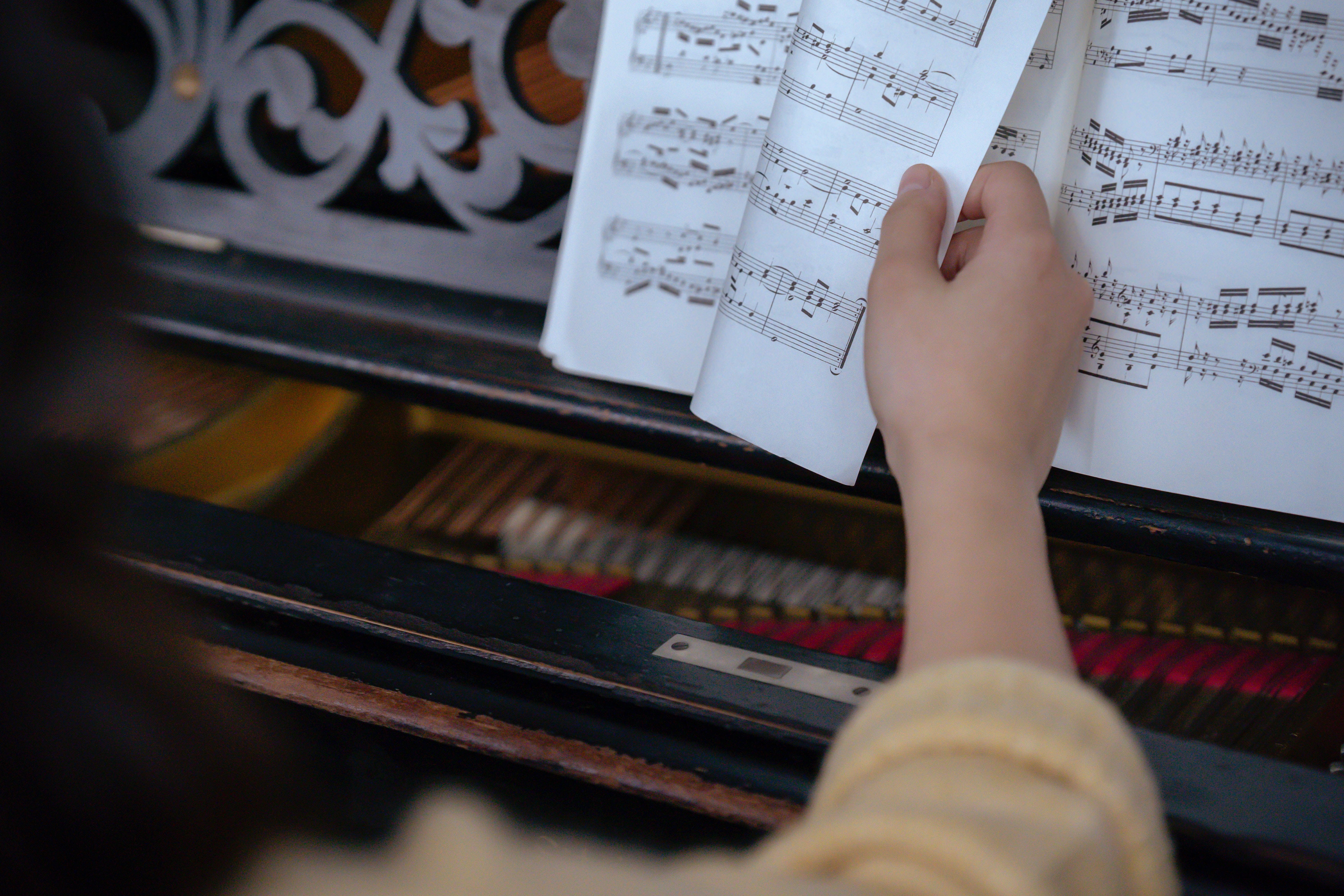 A hand turning the page of a book of music in front of a piano.
