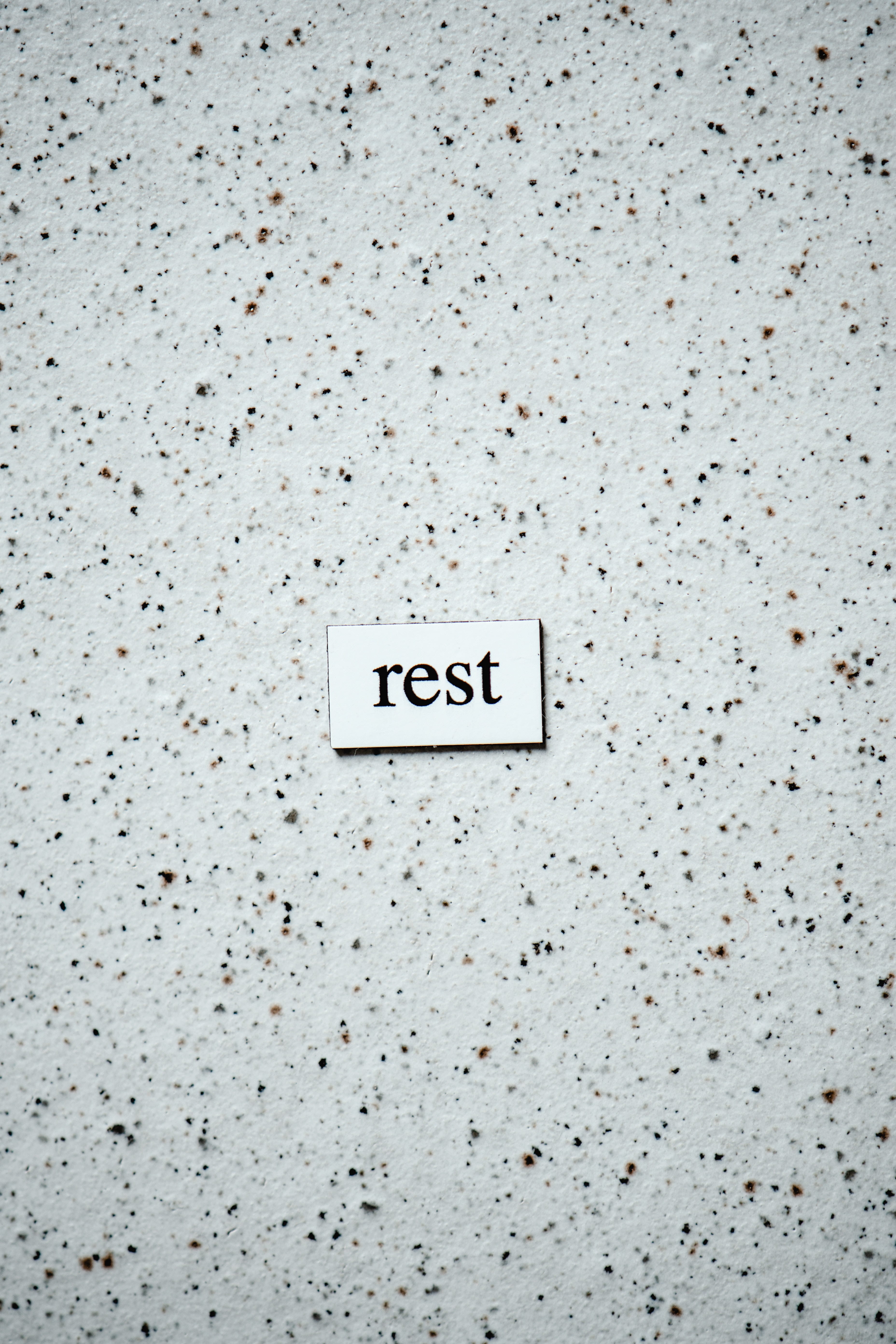 The small white square with the word 'rest' on a background of a white surface dappled with brown and black spots.
