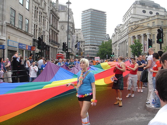 People at London Pride with hundreds of people holding one big pride flag