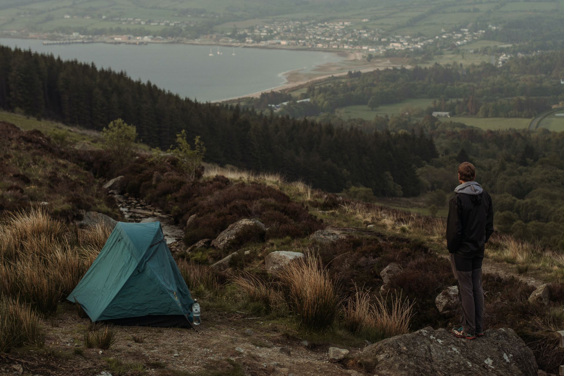 Tent up on the hills, with a man stood watching the view