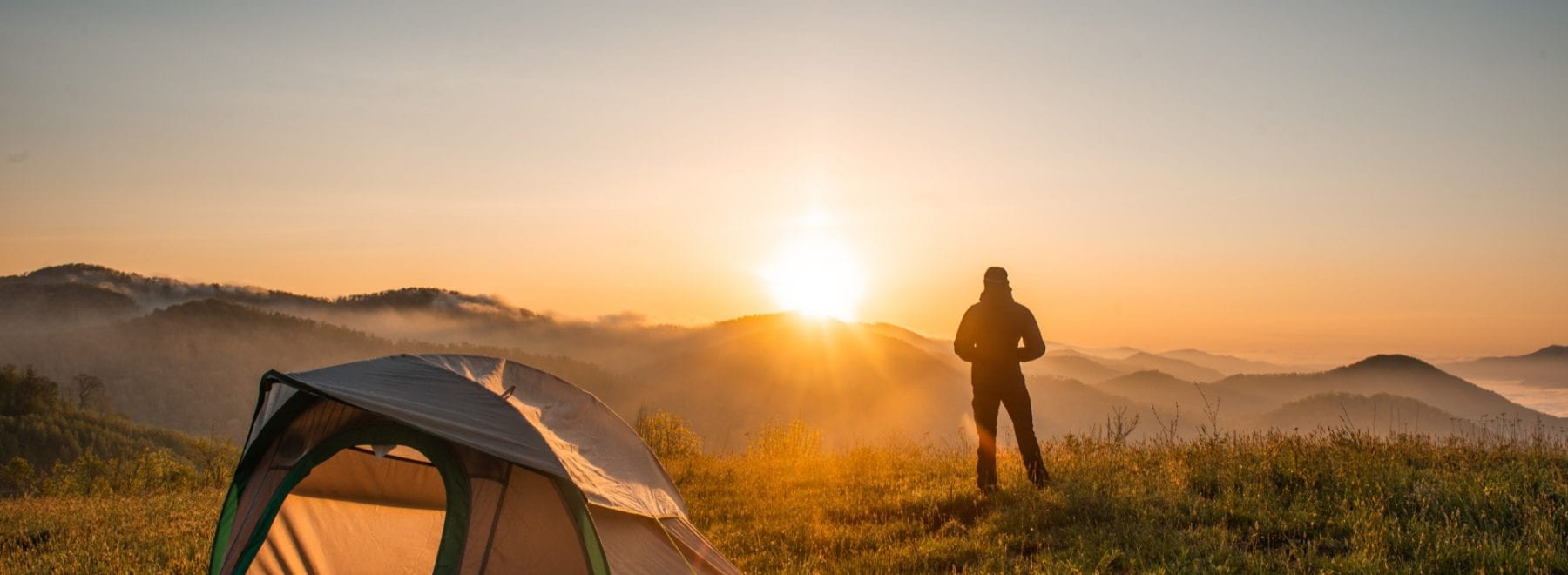 Tent pitched with a man stood watching the sunset
