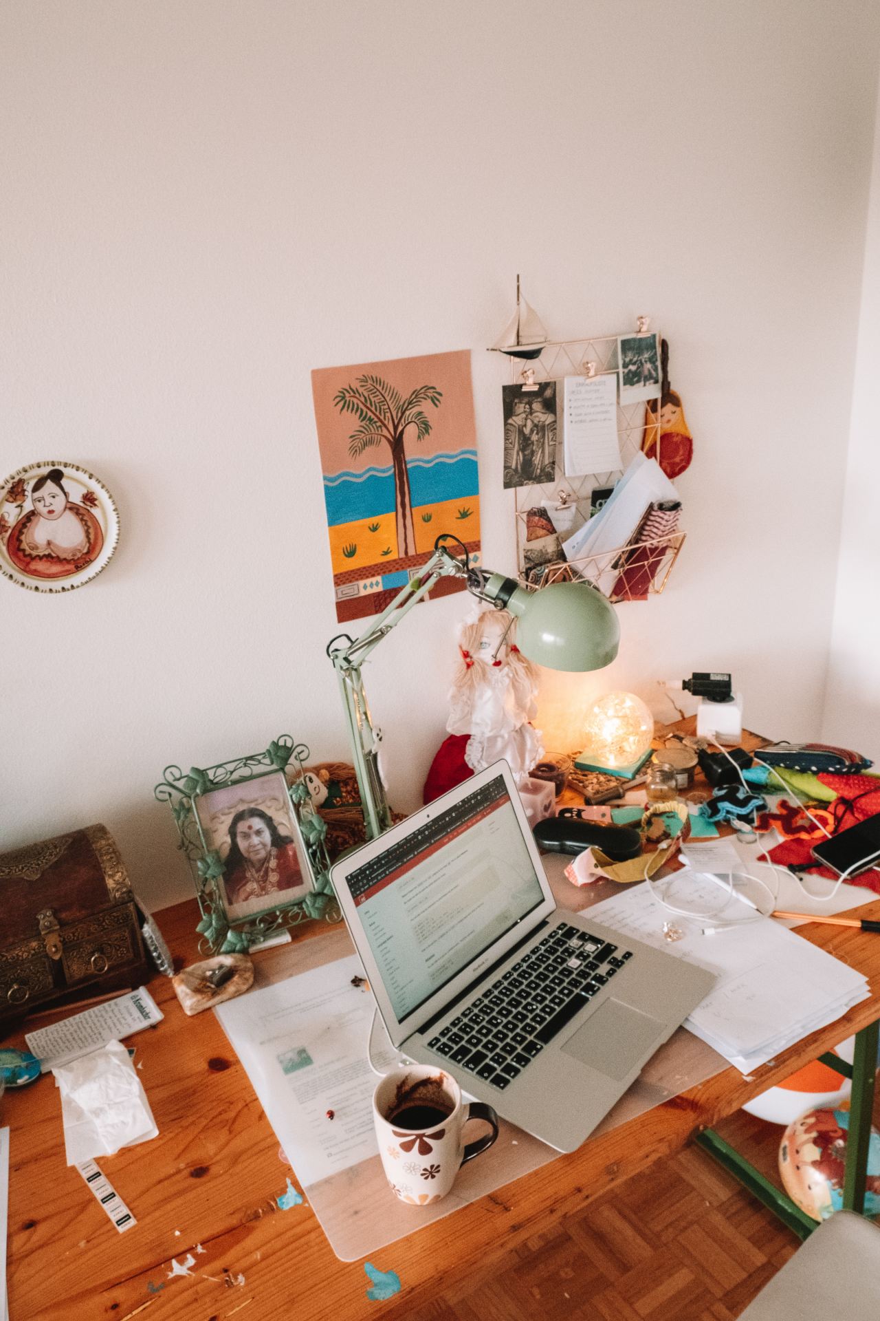 A desk set-up with a laptop, art on the walls and clutter on the desk