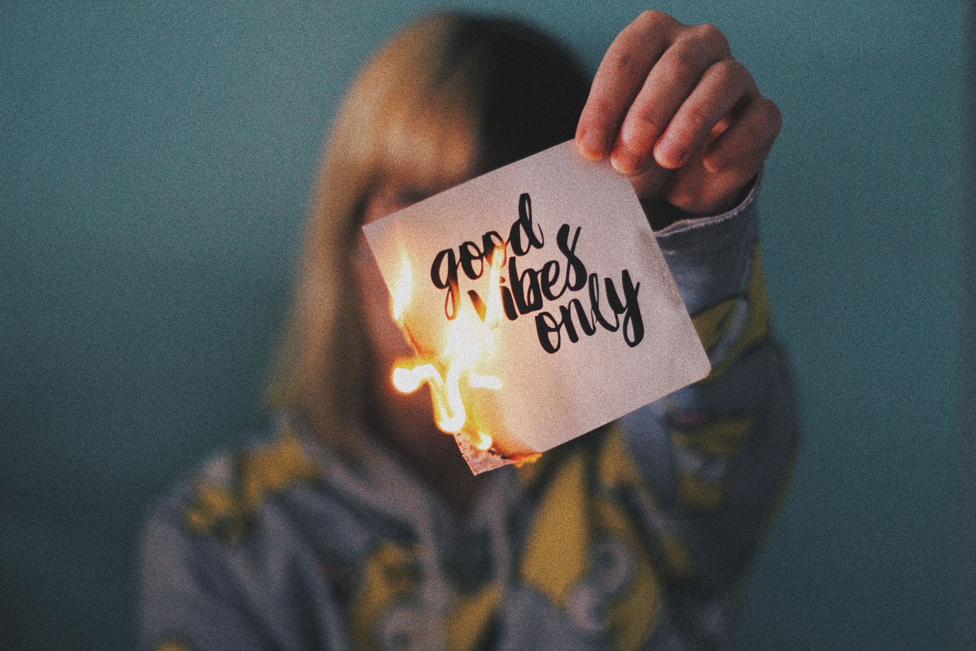 Someone holding a note in front of their face. The note reads 'good vibes only'. It is on fire.