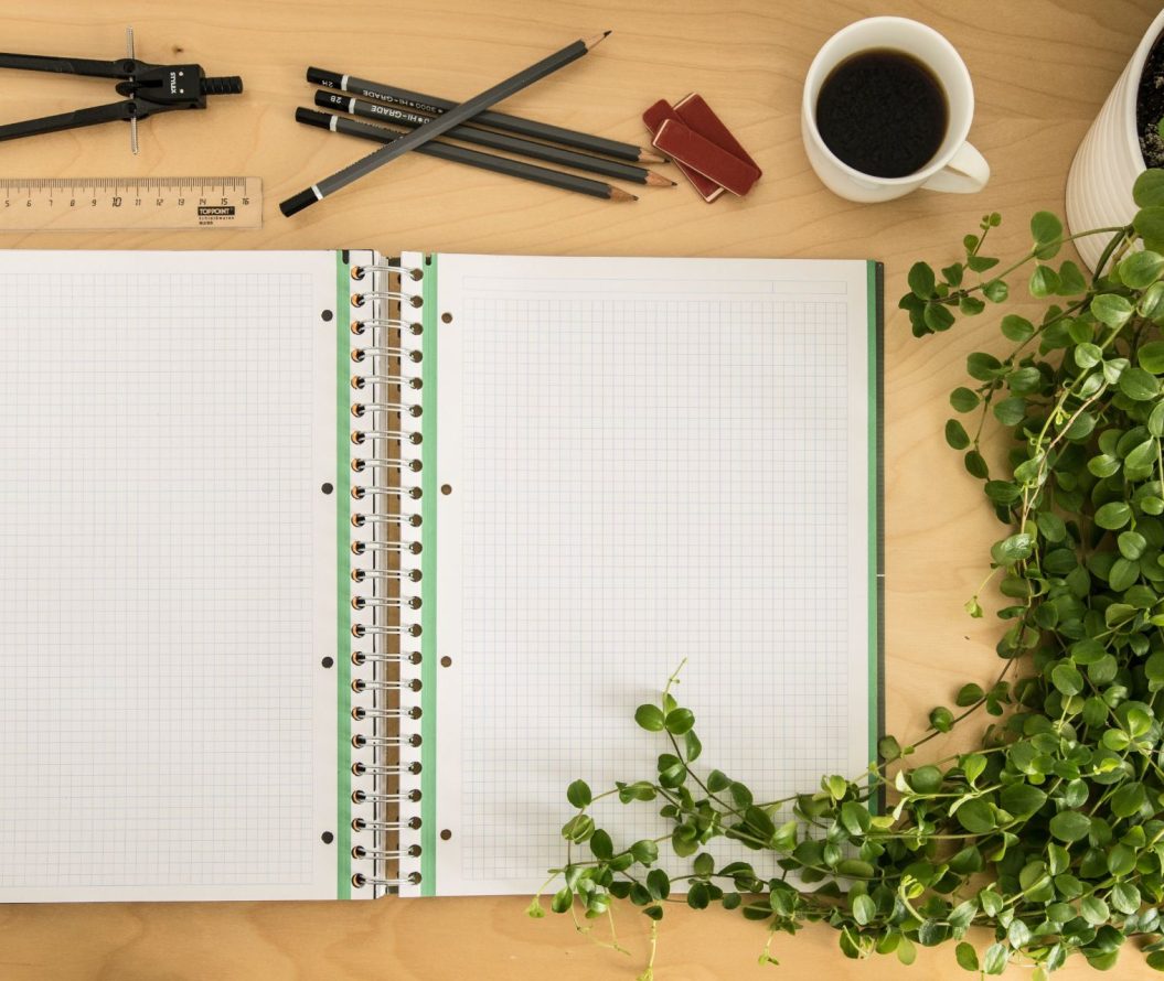 A blank notebook surrounded by pencils and plants